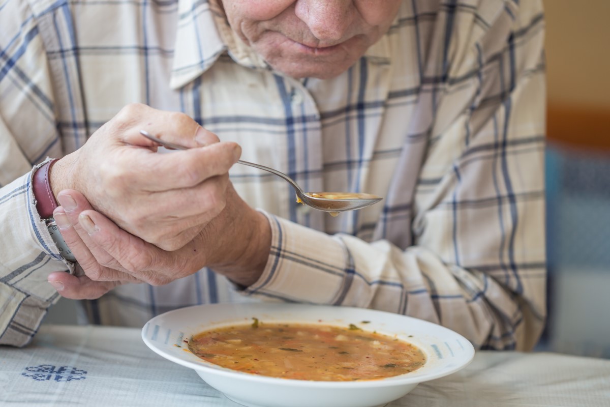 Man äter soppa och håller handen mot skakningar i Parkinsons sjukdom