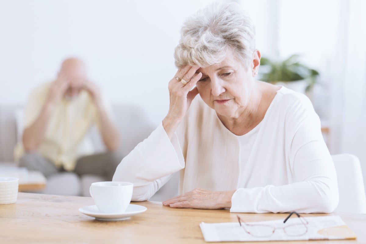 Äldre kvinna håller huvudet, på grund av försämring av hjärnans neurologiska funktioner, möjligen Alzheimers sjukdom. Äldre kvinna i förgrunden, huvudet böjt, lutar sig mot sin hand