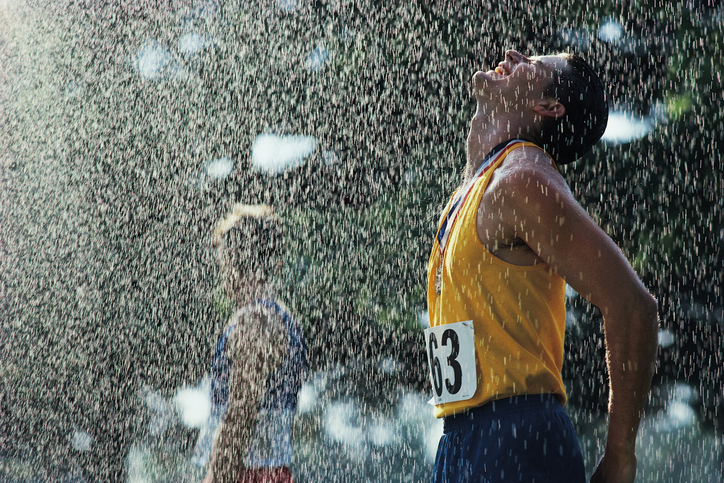 En manlig idrottare efter att ha passerat mållinjen. Det regnar. Hans huvud är vänt uppåt mot dropparna. Han blundar och har en medalj runt halsen. Han bär ett gult linne med siffran 63 på och blå shorts.