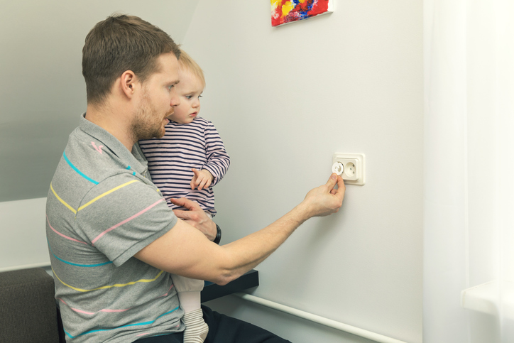 Pappa håller ett litet barn i famnen och stänger kontakten med en elkontakt