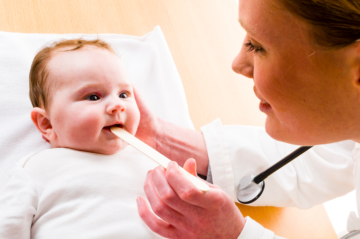 bebis med öppen mun, mamma tittar ner i halsen med en klubba