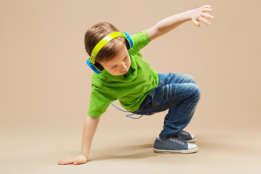 En kille i grön tröja och med hörlurar på sig dansar breakdance