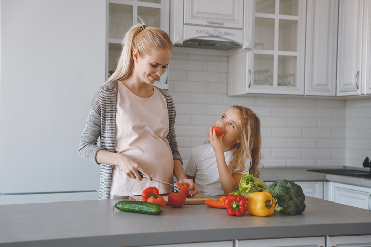 Gravid mamma och dotter lagar en hälsosam måltid i köket.