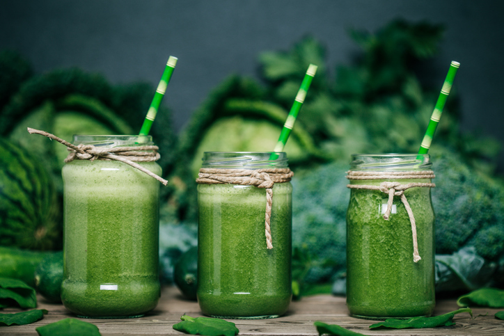 Grön grönsakssmoothie, tre glas, kål, broccoli och ärtor i bakgrunden