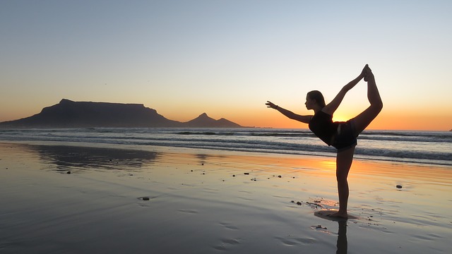 En kvinna utövar yoga på stranden. Solen har gått ner. Det är fortfarande ljust. Hon står på ett ben. Det är lågvatten. Sanden ligger under ett tunt lager av vatten.