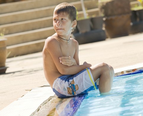 Pojken sitter vid poolen med fötterna i vattnet. Han är kall.