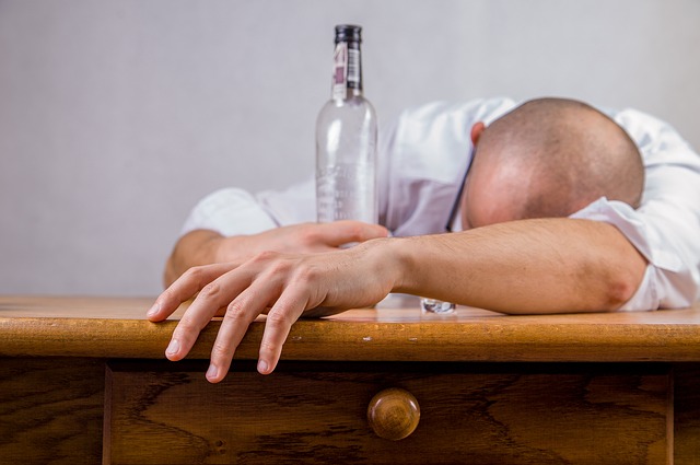 Alkoholism är orsaken till humörstörningar, en man ligger på ett bord med en tom flaska alkohol i handen, en alkoholist