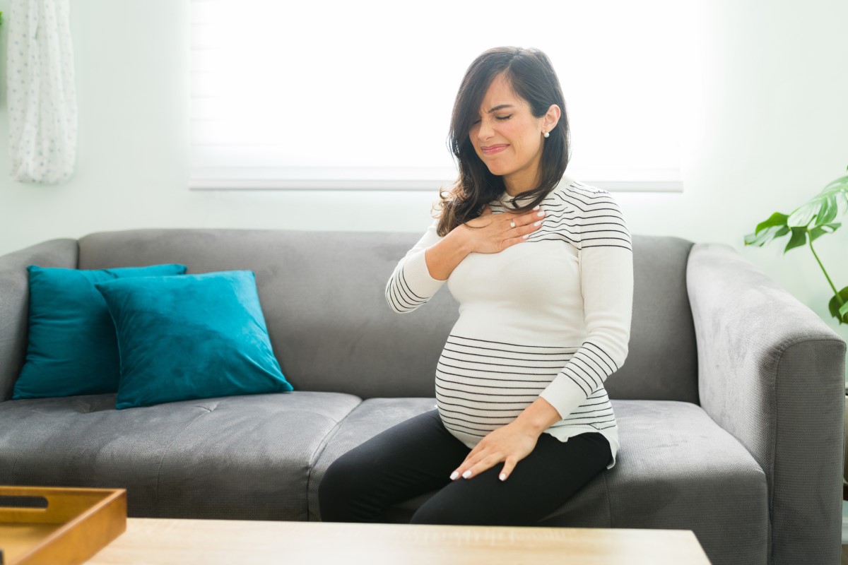 Halsbränna är vanligt hos gravida kvinnor - en gravid kvinna sitter i en soffa och håller sig för bröstet